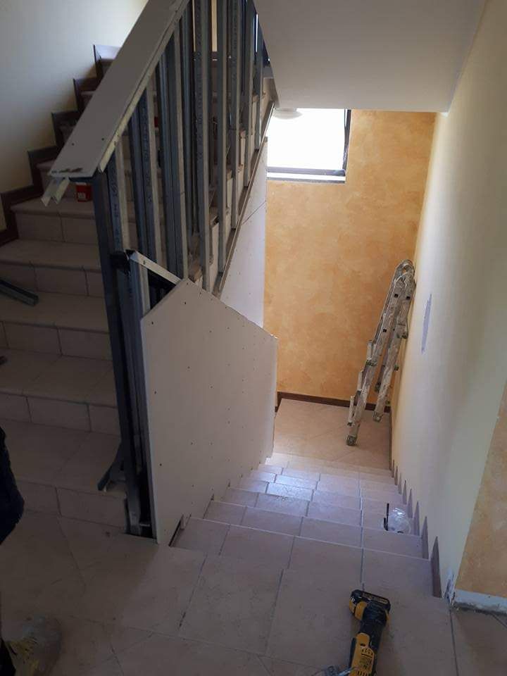 Scala con ringhiera in costruzione; pareti beige chiaro; scala appoggiata a una parete arancione; pavimenti piastrellati.