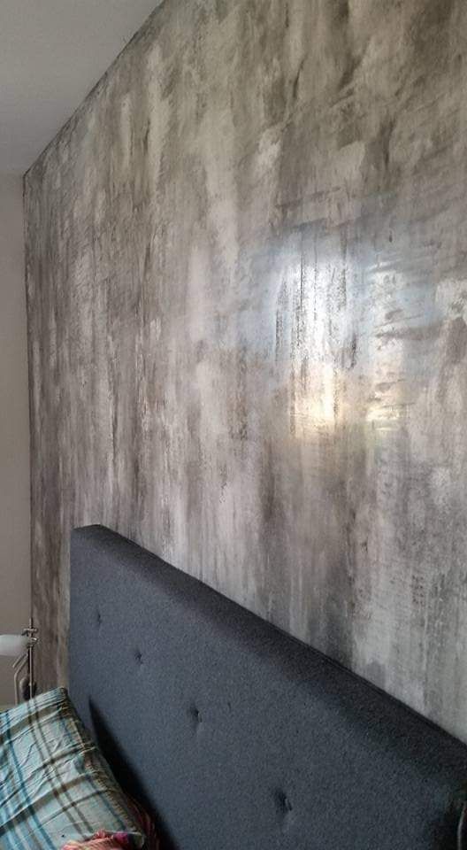 Parete grigia e bianca con texture dietro una testiera imbottita grigio scuro in una camera da letto.