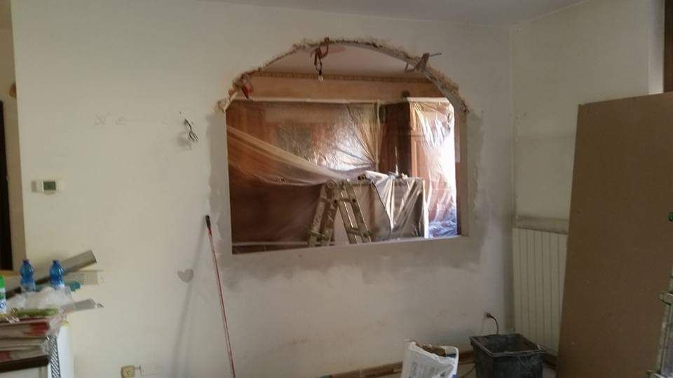 Parete in fase di ristrutturazione con apertura ad arco rivestita in plastica; scala visibile all'interno.