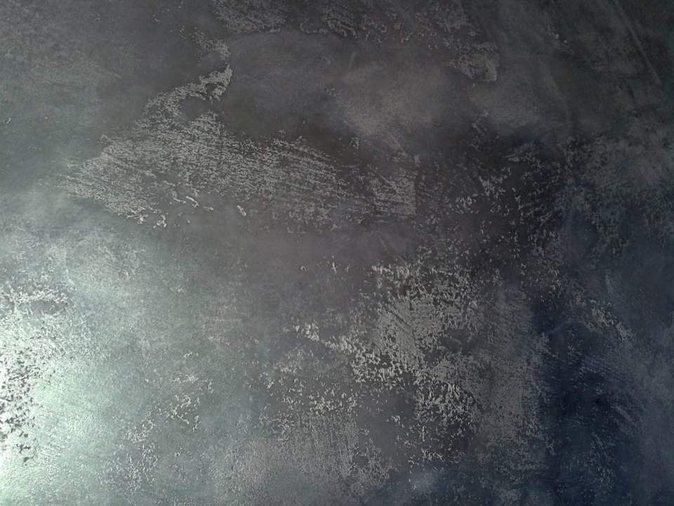 Parete grigio scuro testurizzata con macchie argentate che riflettono la luce.