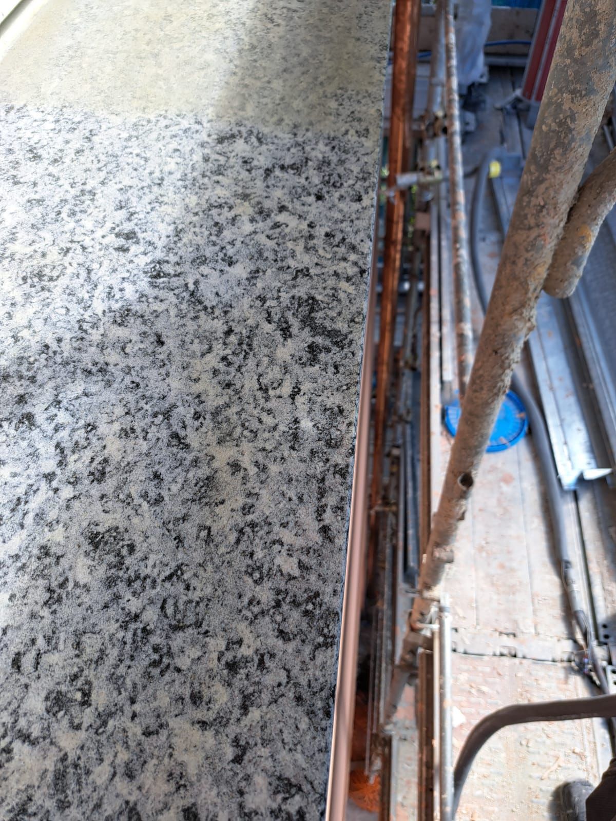 Primo piano di un piano di lavoro in granito accanto a un'impalcatura arancione e metallica.