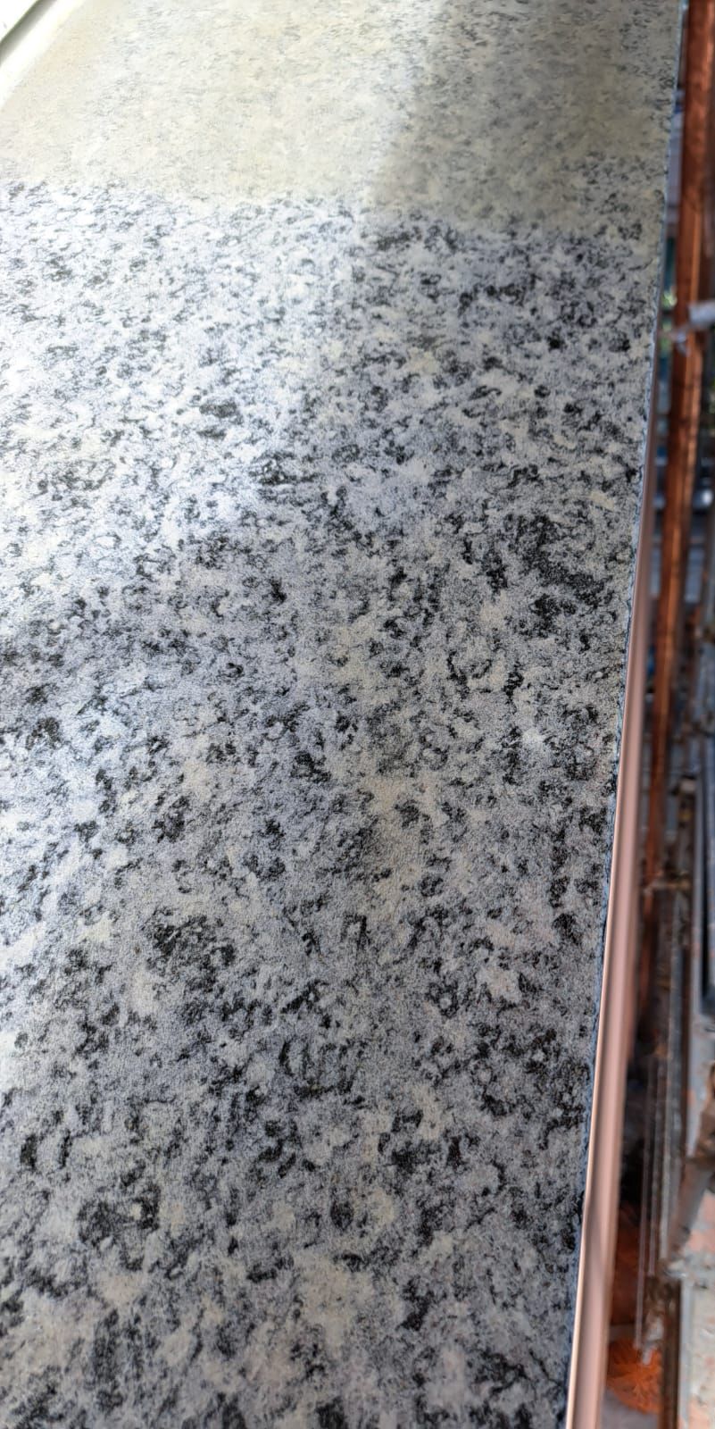 Piano di lavoro in granito con macchie nere, accanto a un bordo marrone.