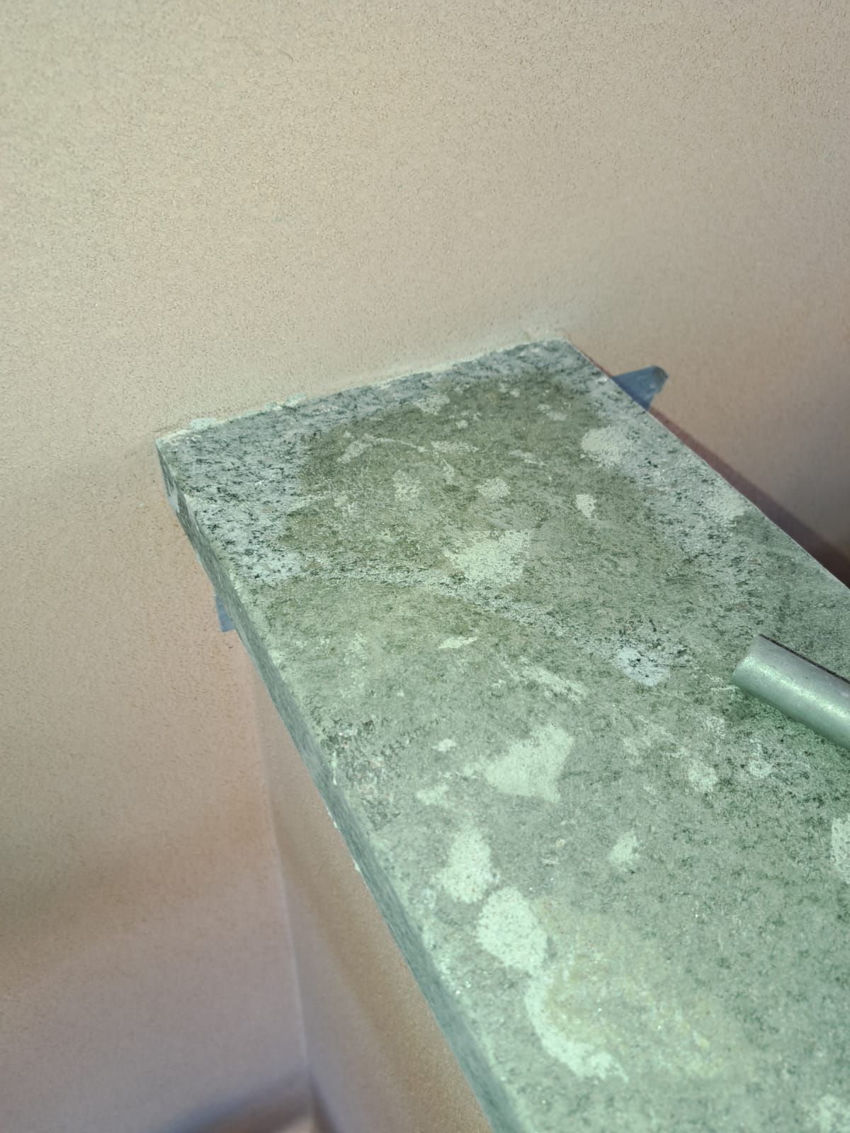 Primo piano di una sporgenza di cemento grigio usurato contro un muro rosa chiaro.