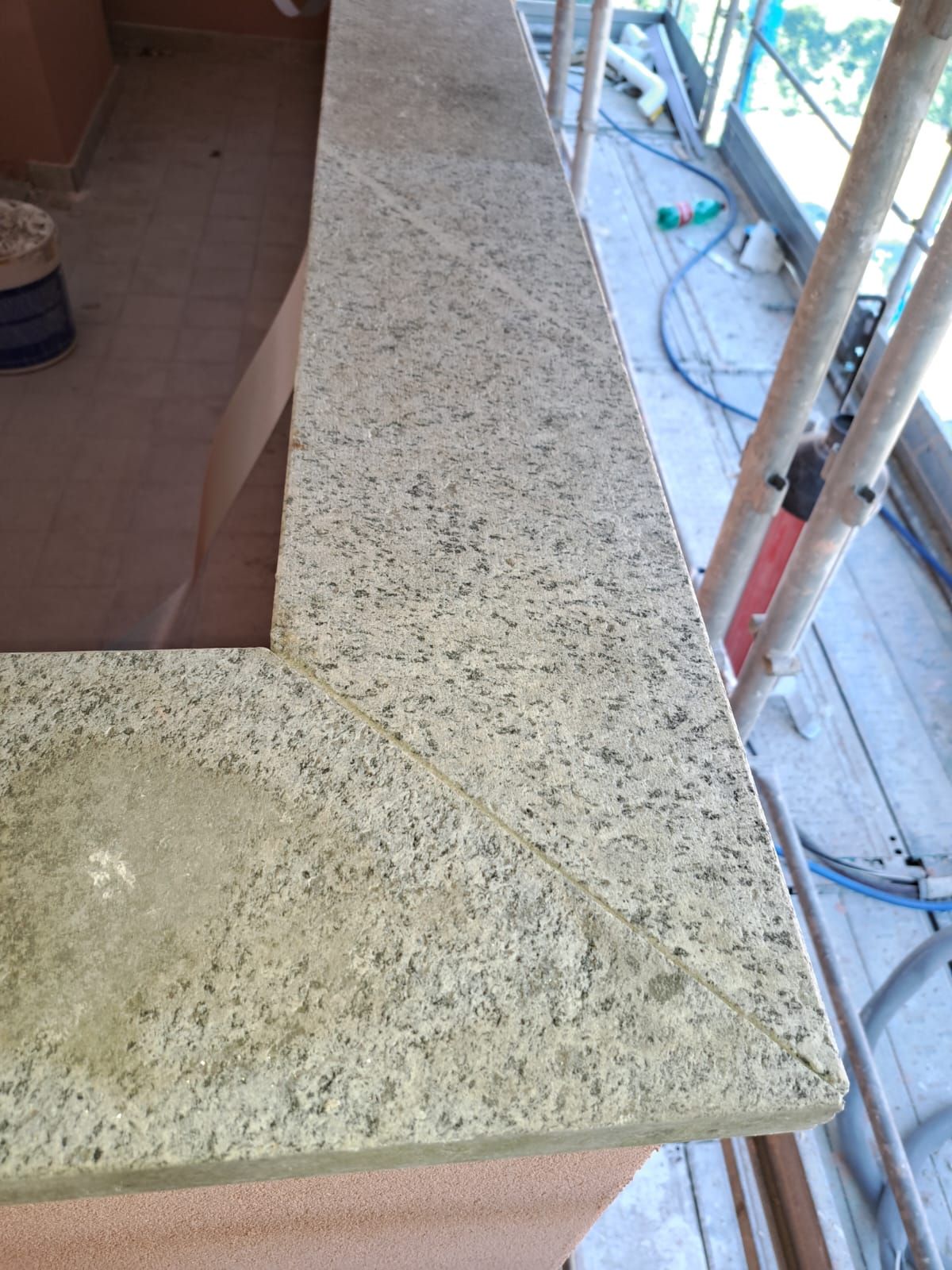Primo piano di un piano di lavoro in granito chiaro con macchie visibili; su un balcone in costruzione.