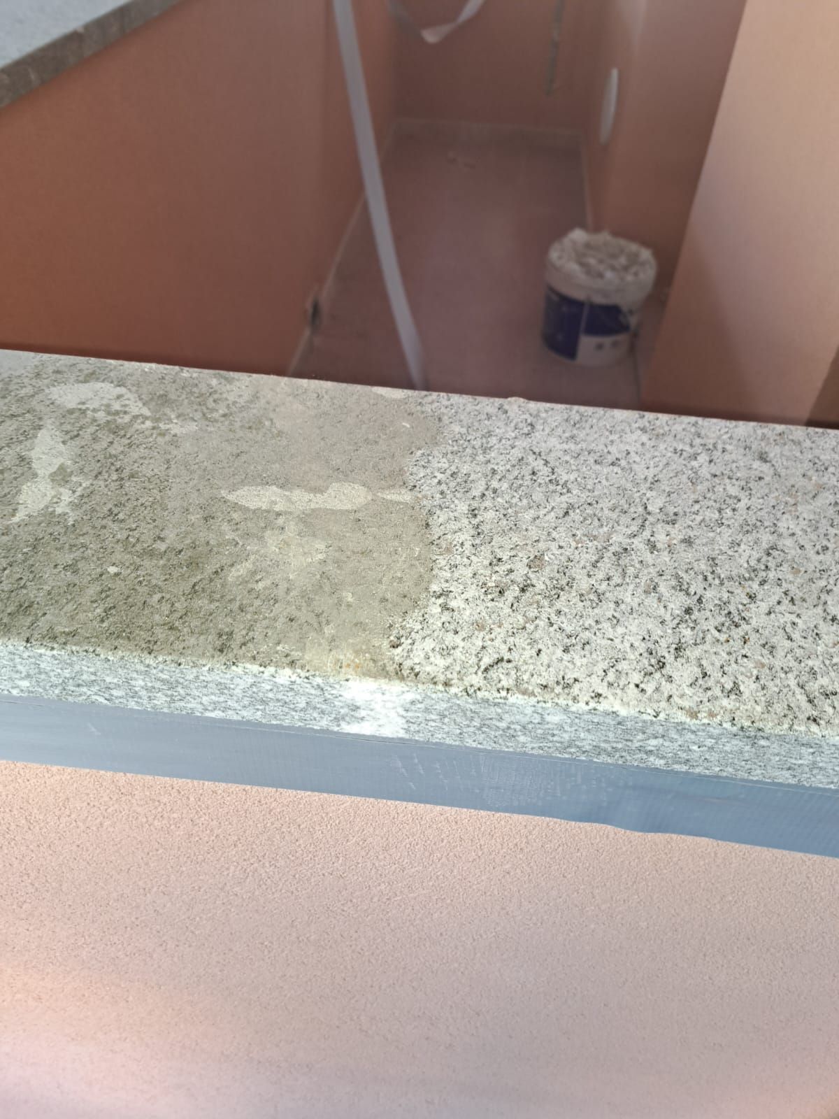 Piano di lavoro in granito, mezzo pulito, con parete rosa sottostante e corridoio interno sullo sfondo.