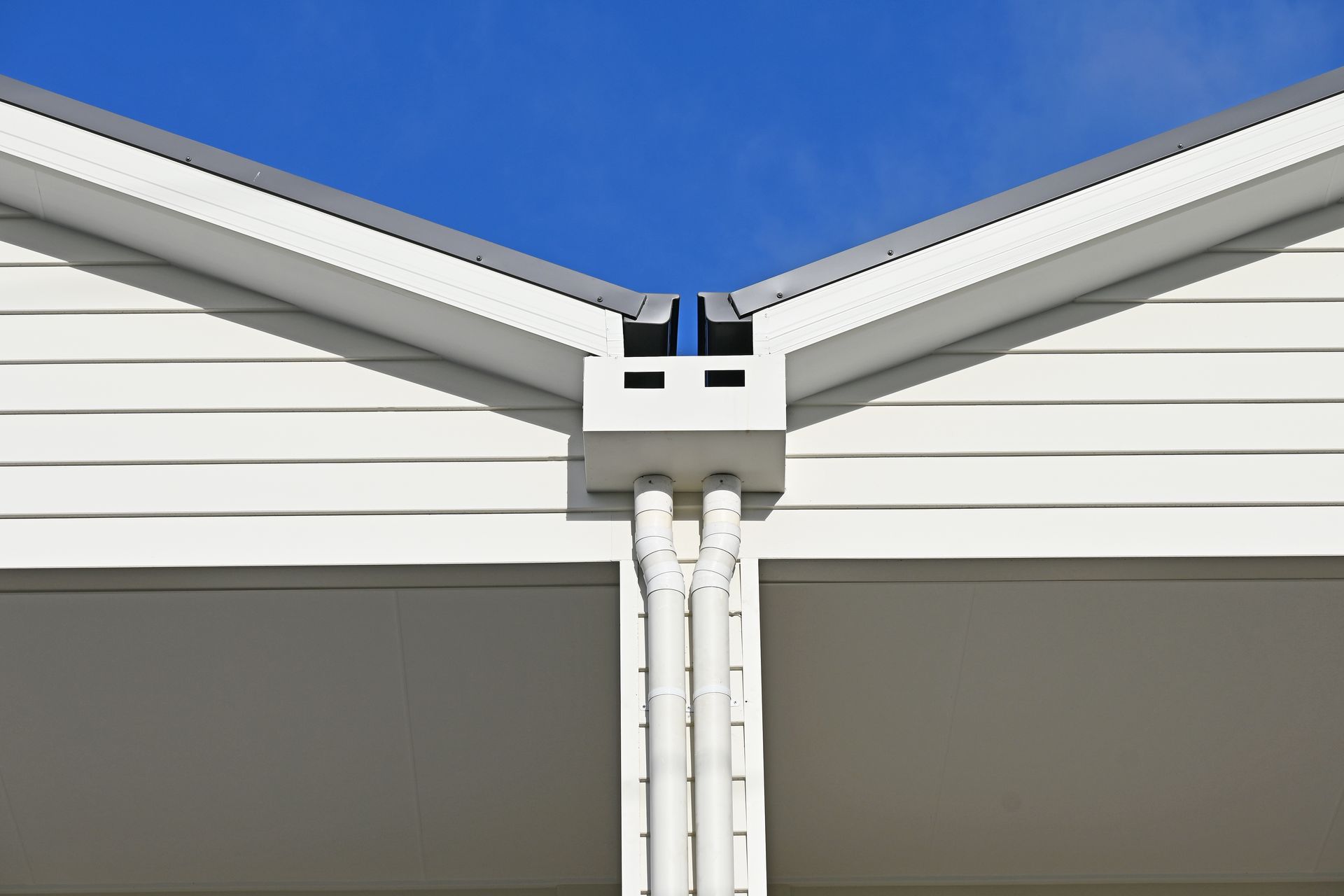 White house corner with gutters and downspouts against a bright blue sky.