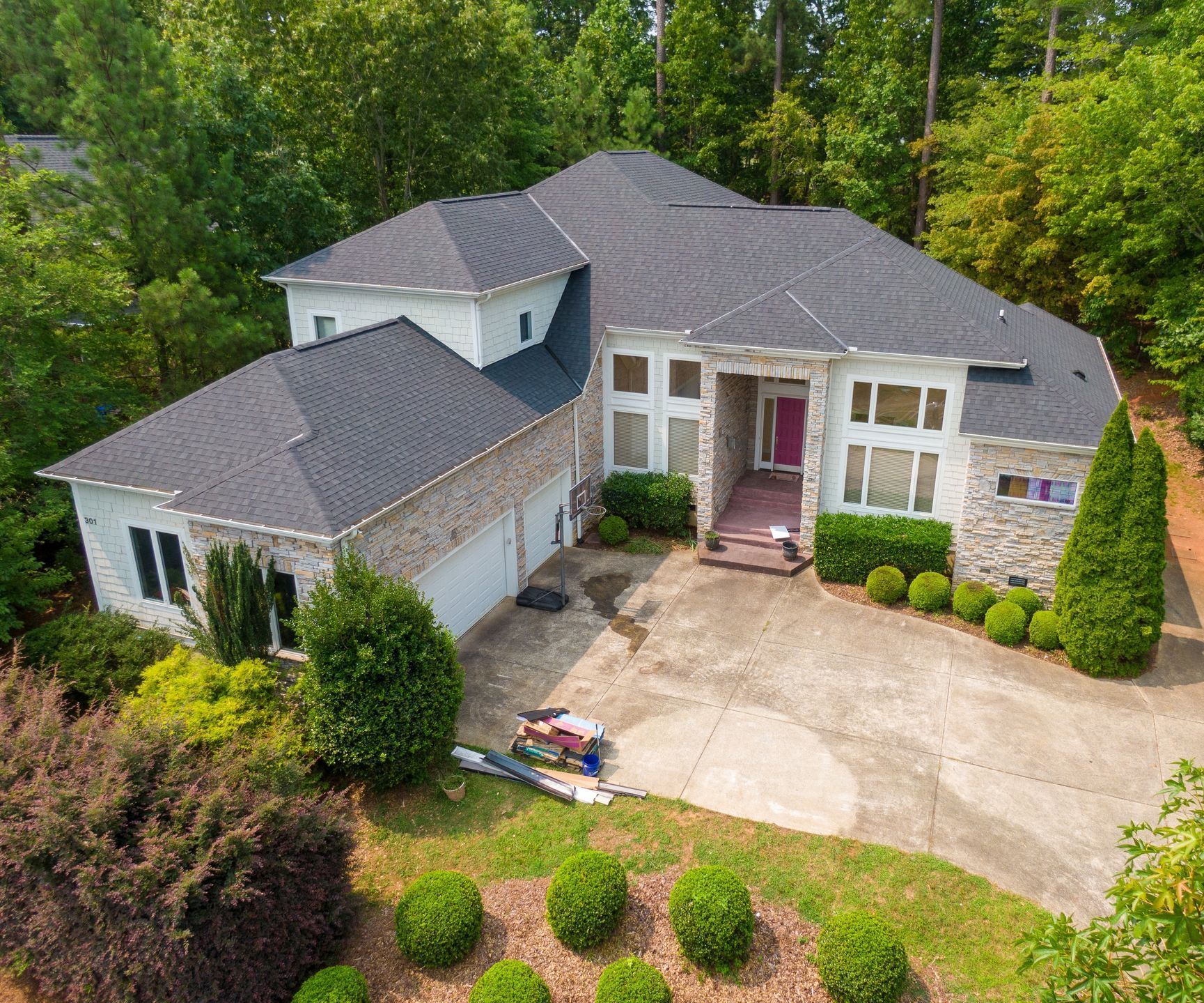 Two-story house with gray roof, white and stone exterior, three-car garage, and landscaped yard.