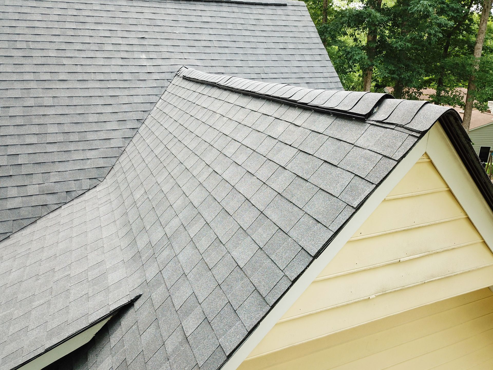 Gray asphalt shingle roof on a house, angled view, yellow siding below.