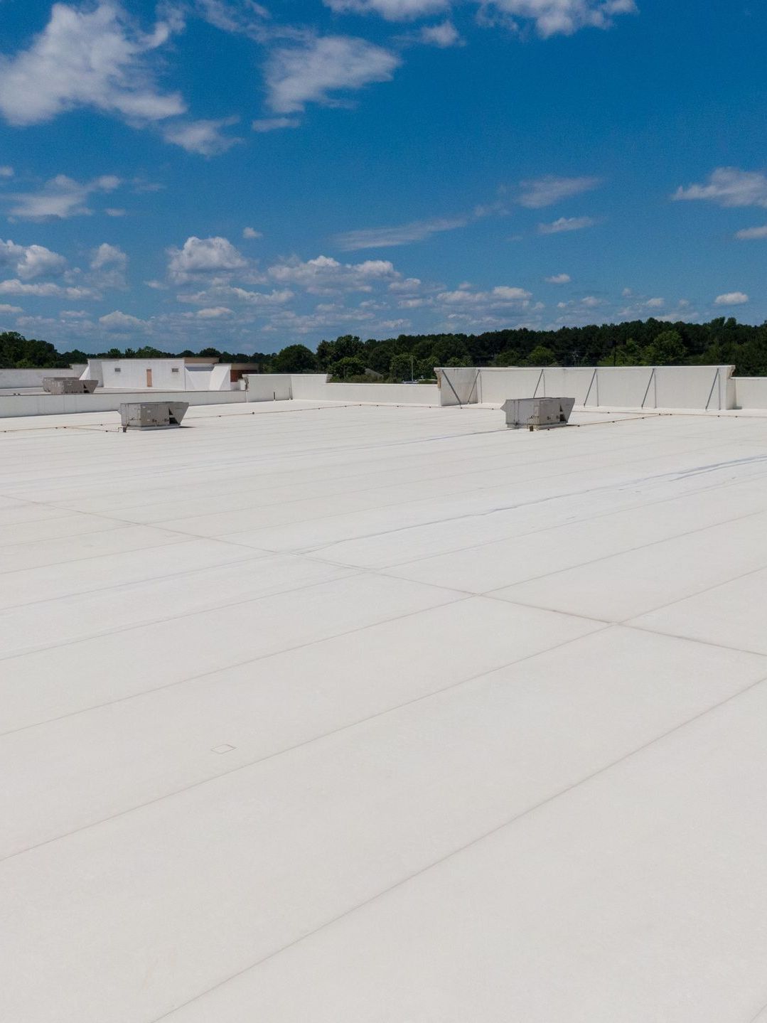 White flat roof with vents against a bright blue sky with scattered clouds.