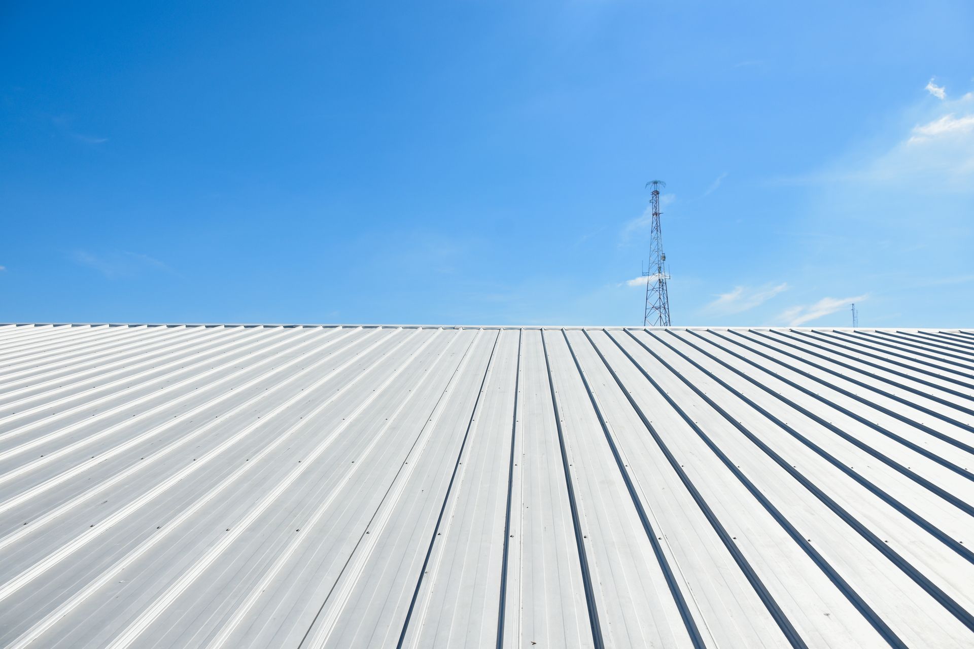 Silver corrugated metal roof with blue sky and radio tower.