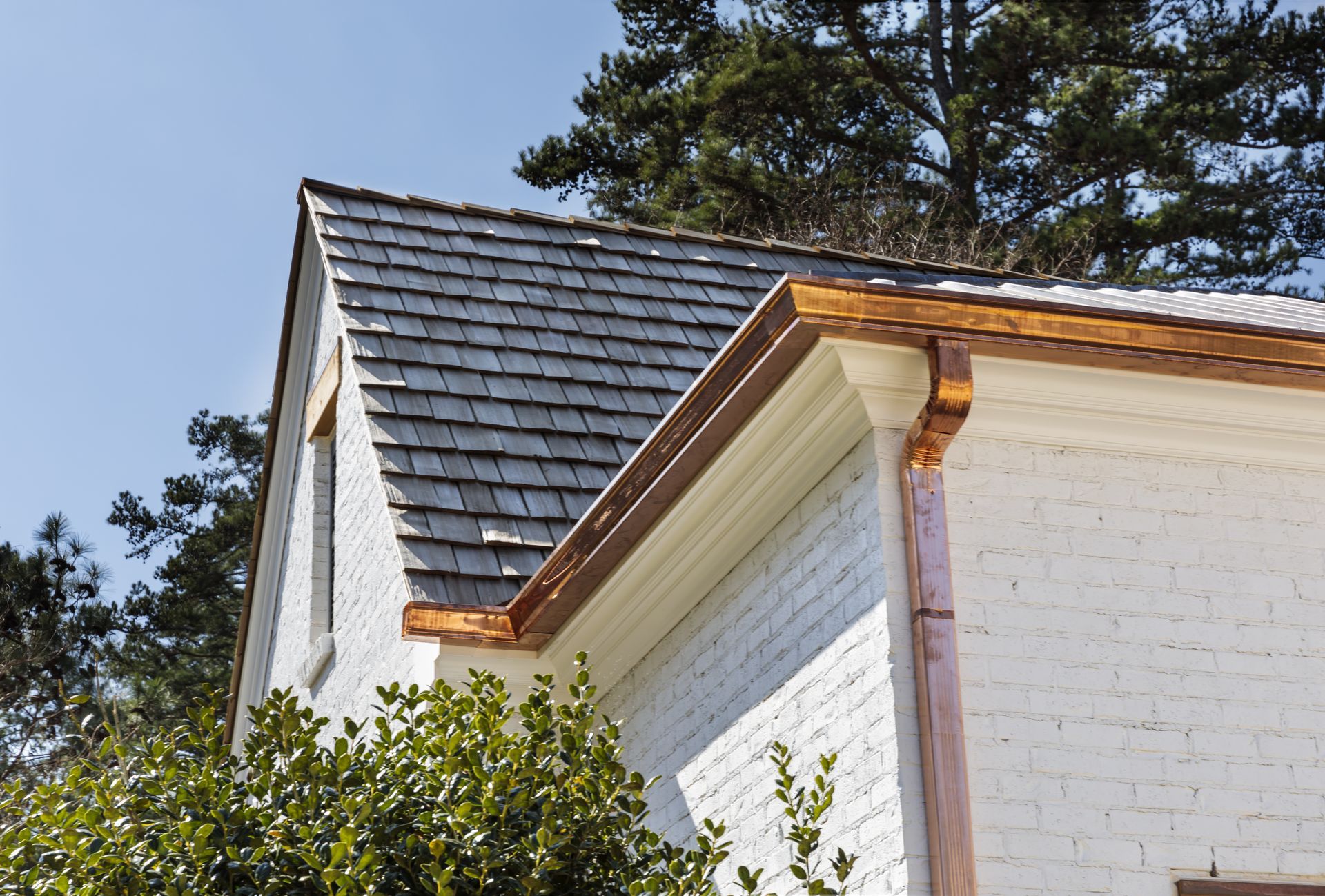 White brick building with copper gutters and gray shingle roof under a blue sky.