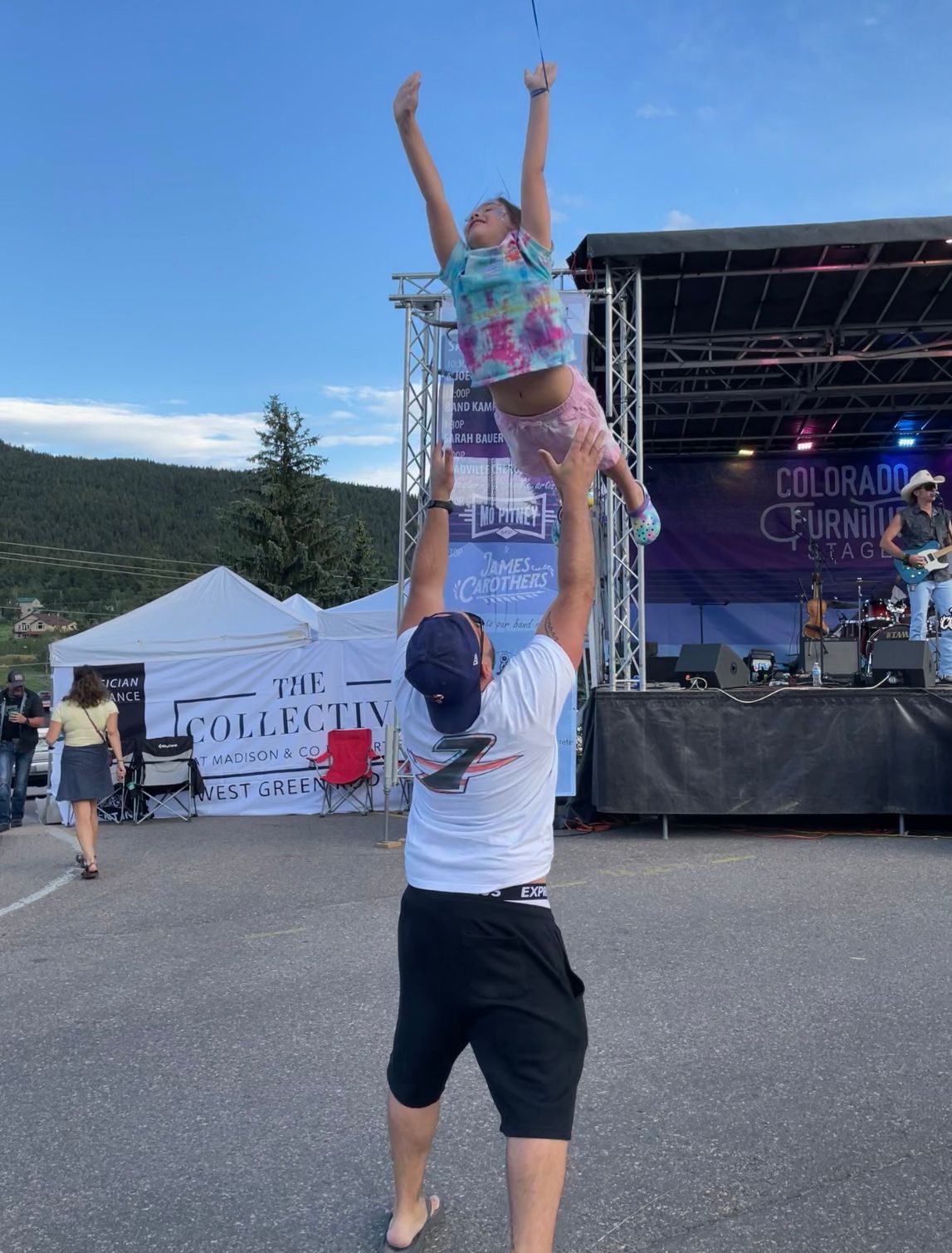 A man is holding a little girl in the air in front of a stage.
