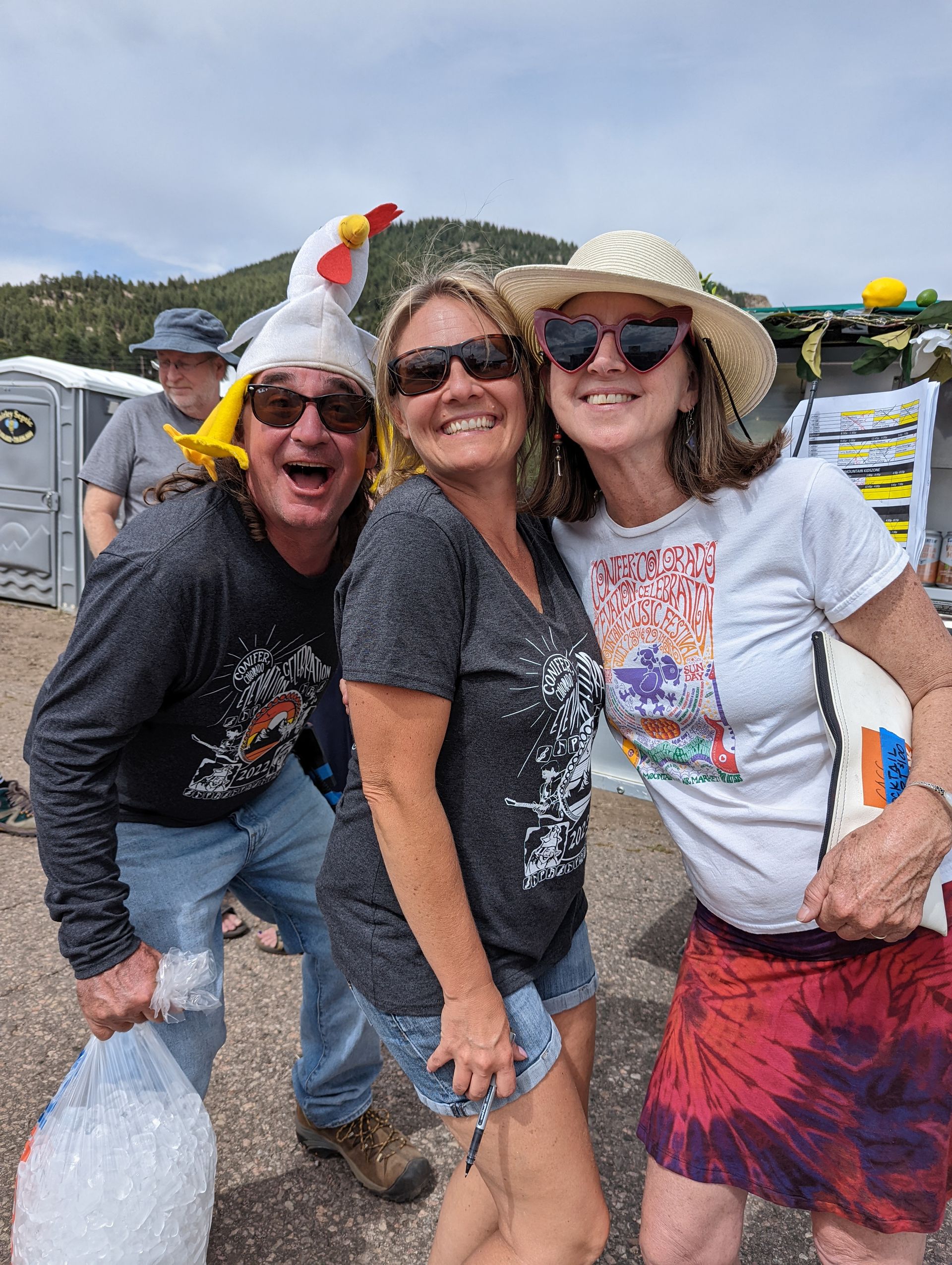 A man and two women are posing for a picture together . one of the women is wearing a chicken hat.