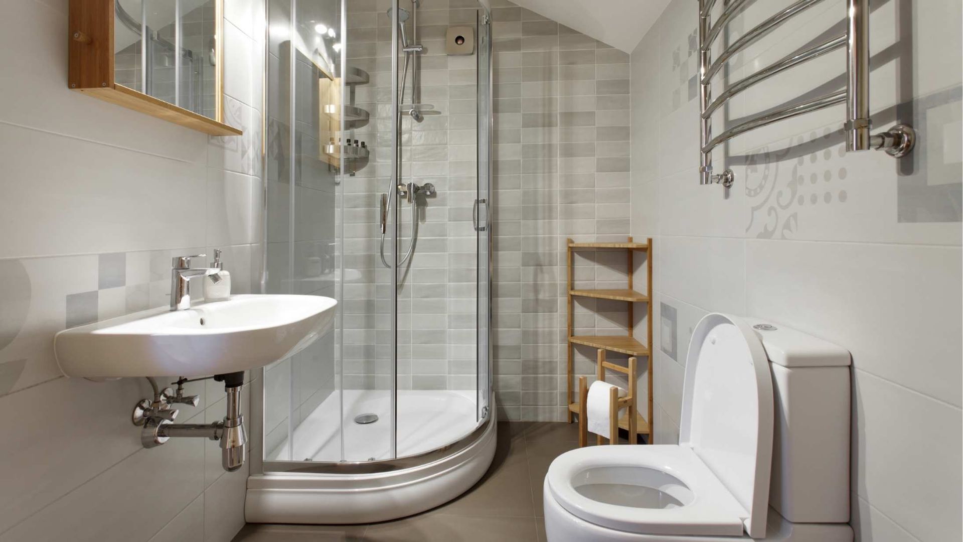 Small bathroom with a white sink, shower, and toilet, with light gray tiled walls.