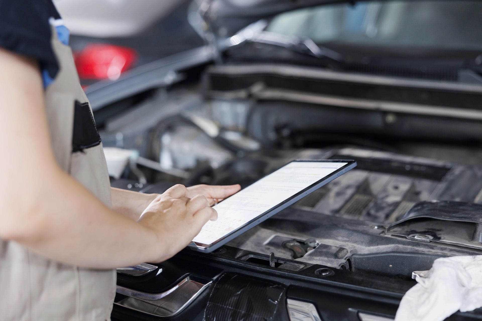 A mechanic is looking at a clipboard under the hood of a car.
