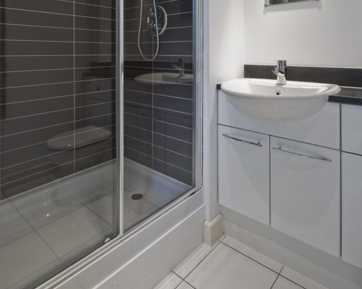 Modern bathroom with gray tiled shower and white vanity with a rounded sink.