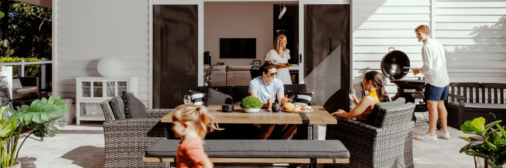 Family and friends enjoying a barbecue on a patio, with a child in the foreground.