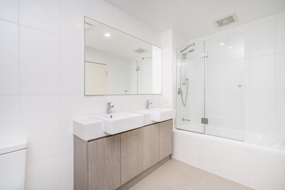 Modern white bathroom with double sink vanity, large mirror, and glass shower enclosure.