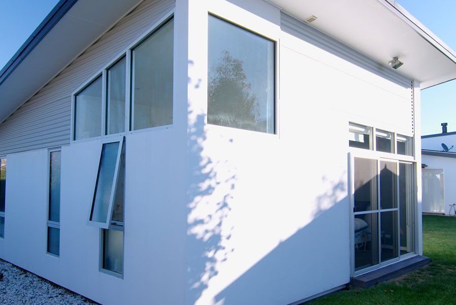 White modern house with large windows and a screen door. One window is open.