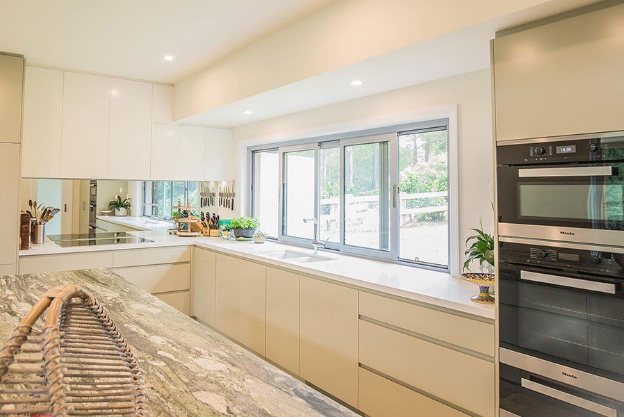 Modern kitchen with light cabinets, marble island, built-in oven, and a large window.