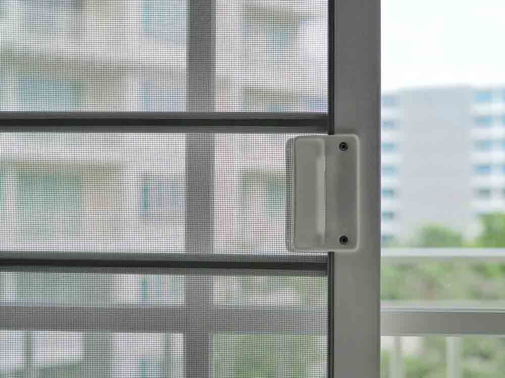 Close-up of a white sliding screen door with a white handle, overlooking a cityscape.