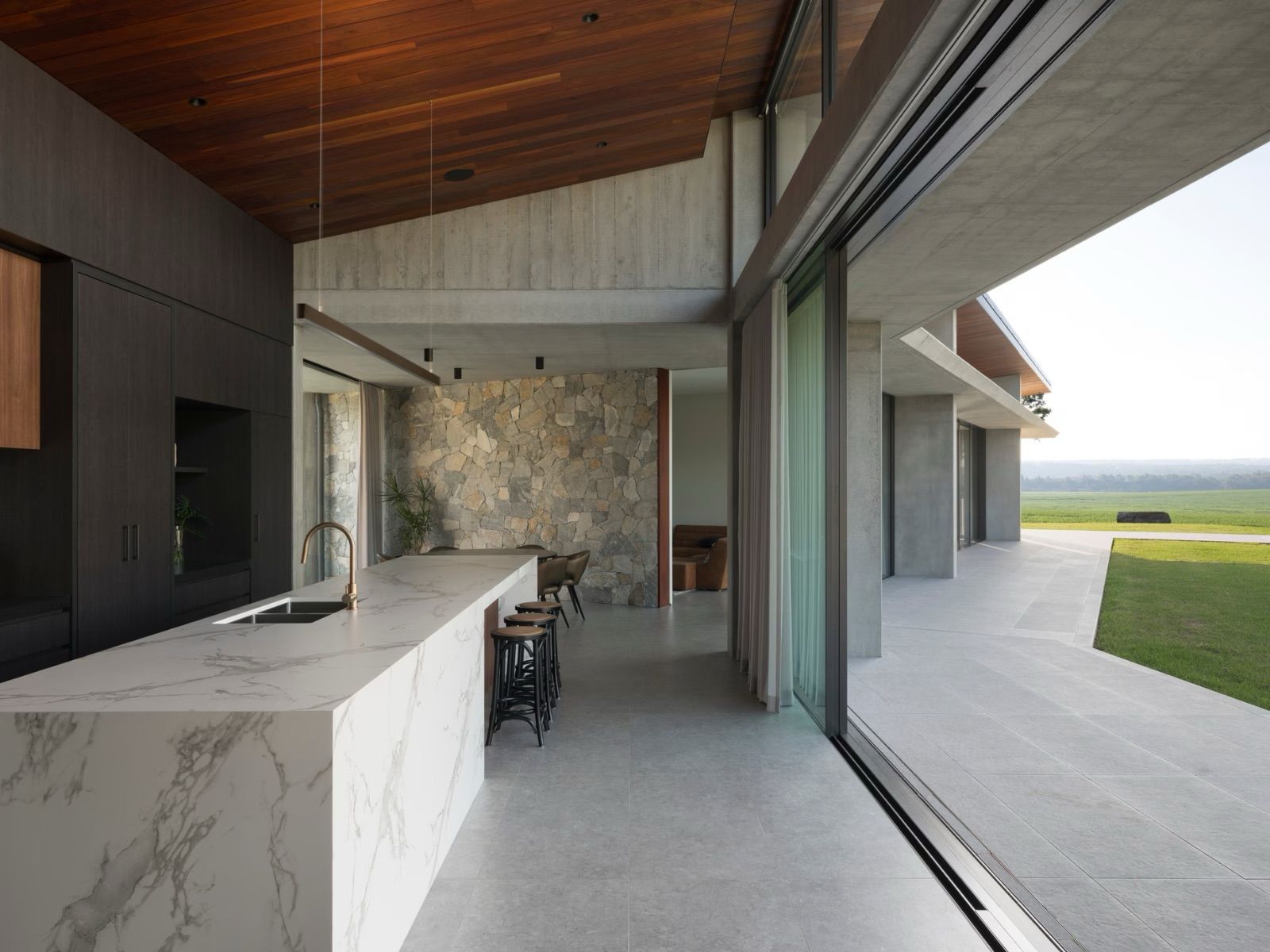 Modern kitchen with marble countertop, wood ceiling, and sliding glass doors to a grassy outdoor space.
