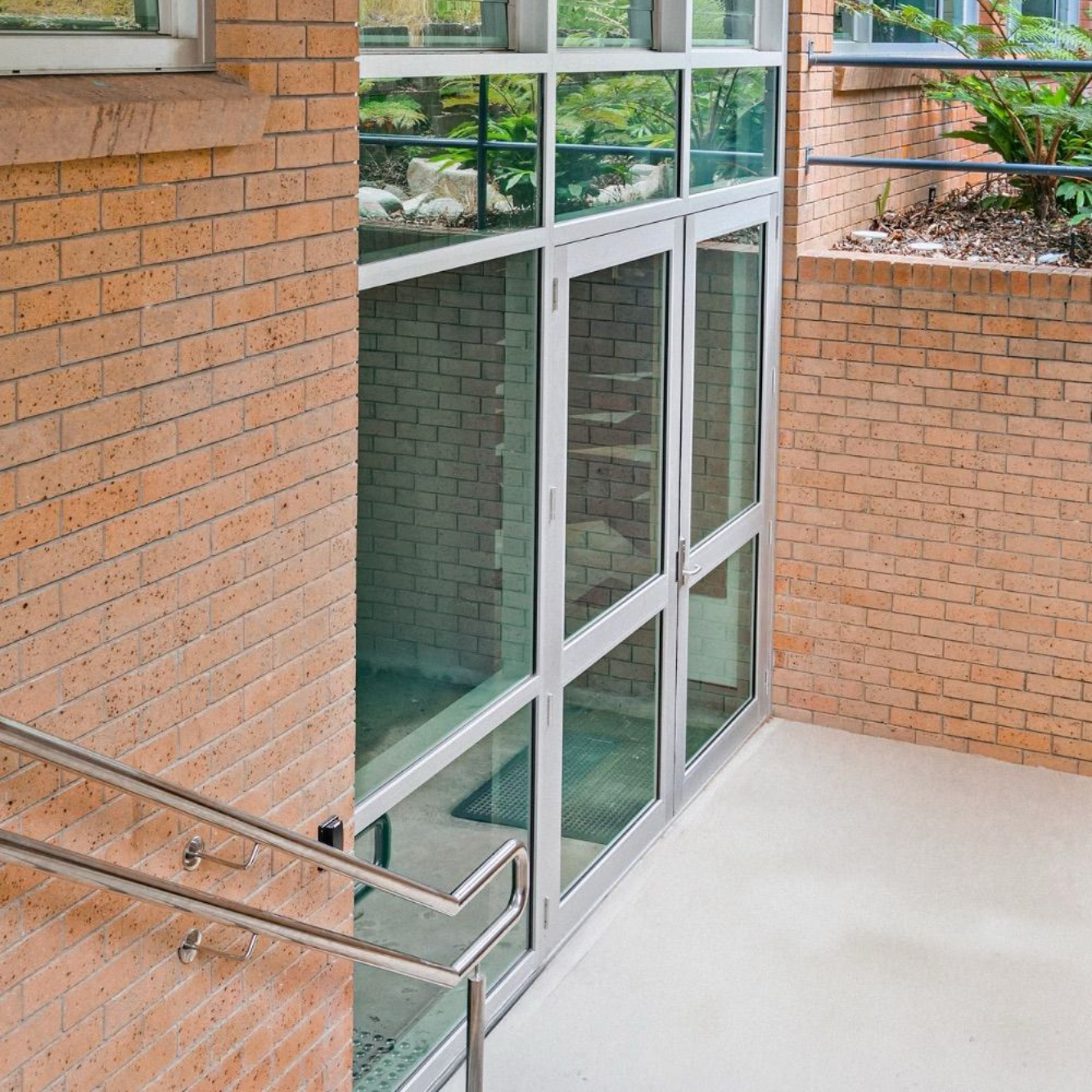 Glass doors and windows in a brick building. Stainless steel handrail next to steps.
