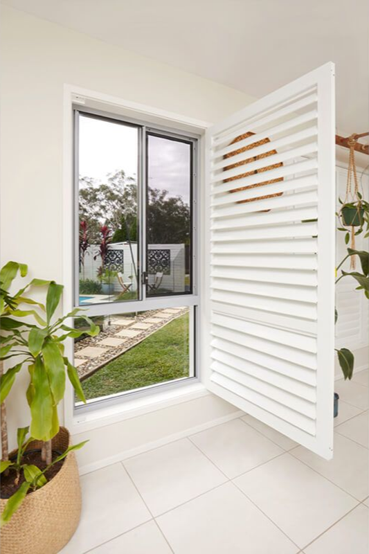 Window with white shutters open, revealing a view of a yard and a pool. A potted plant sits in the corner.