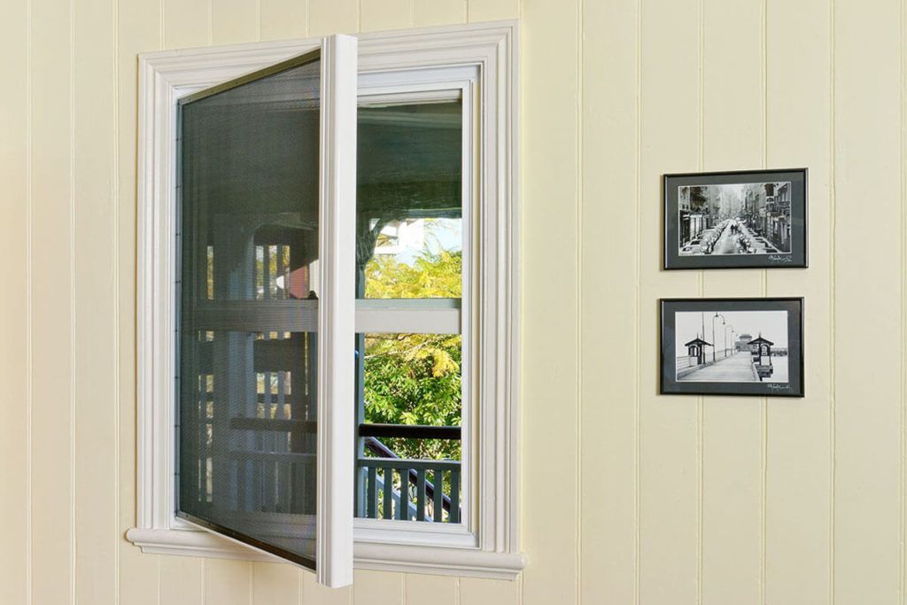 Open window with screen. White trim, yellow siding, two framed black and white photos on wall.