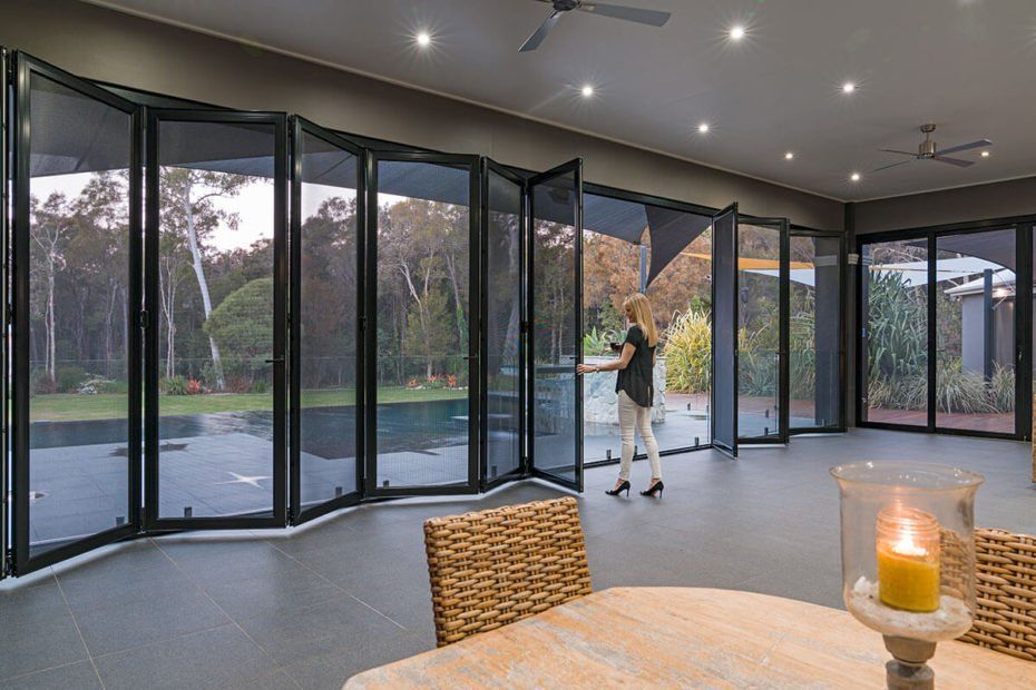 A person opens a large folding glass door with a screen, revealing a backyard pool.