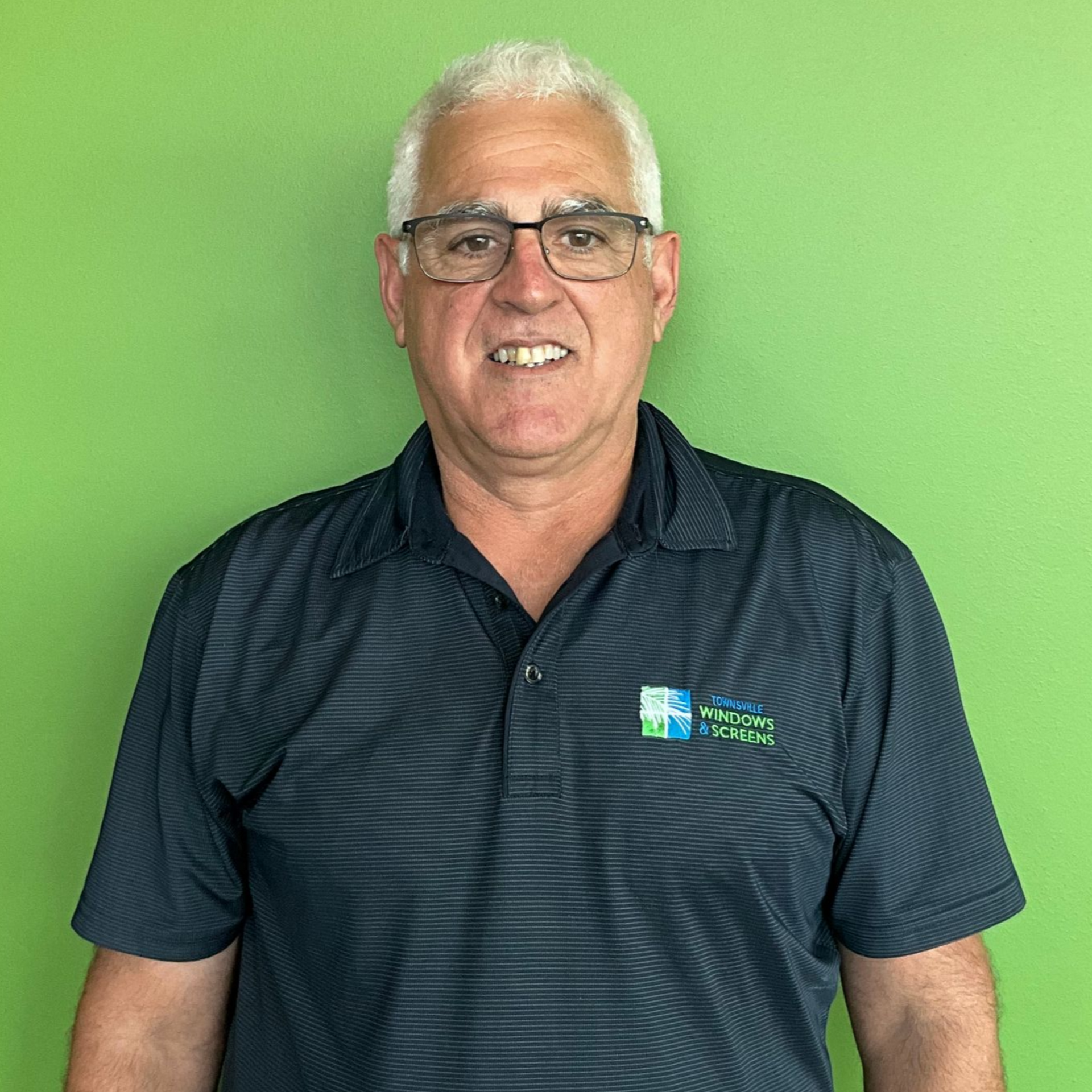 Man with white hair smiles, wearing suit and tie; dark background.