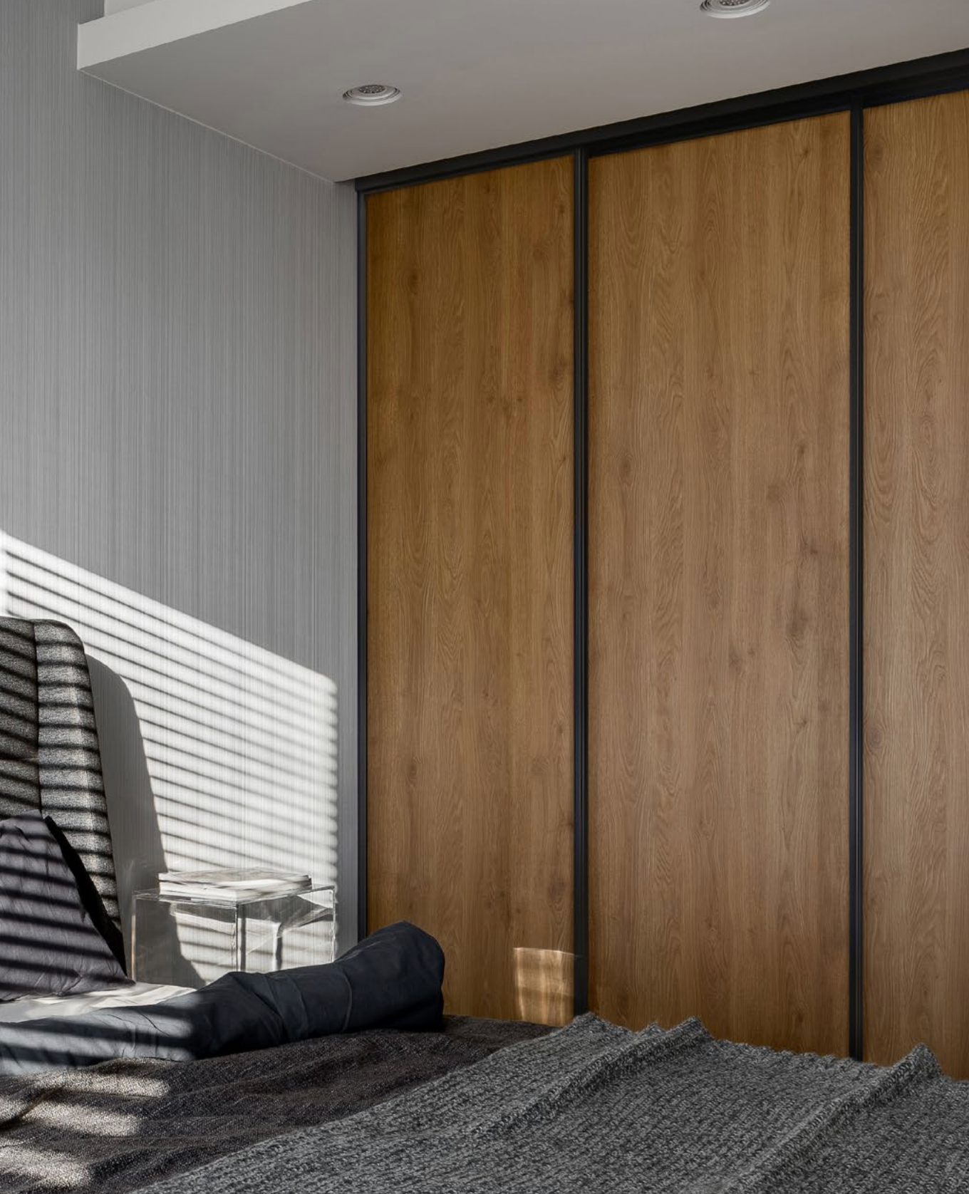 Bedroom with wooden sliding closet doors, bed with blanket and pillow, sunlight.