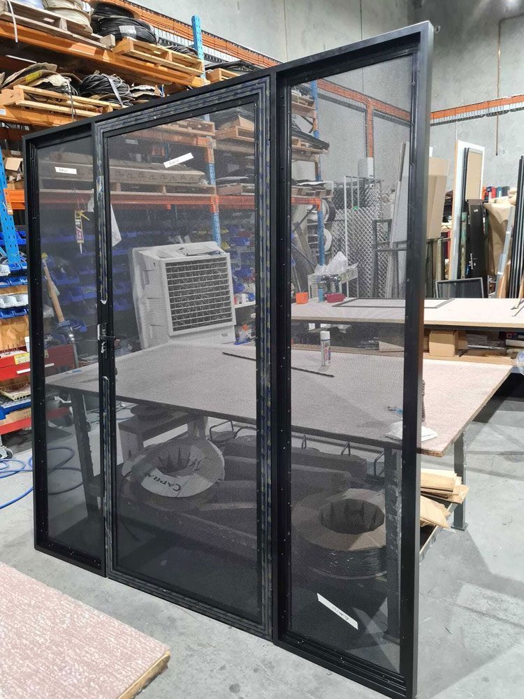 Black screen door set against a workshop backdrop with a desk and industrial equipment.