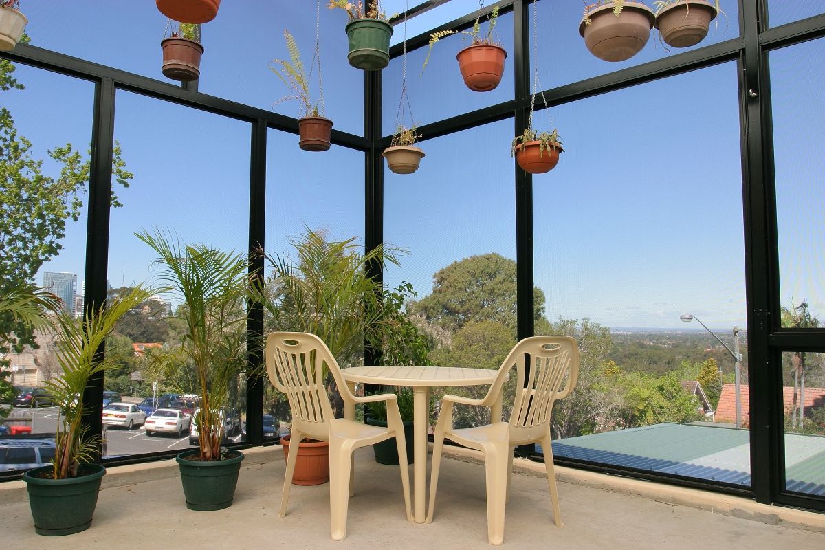 Patio with table, chairs, plants in pots hanging from ceiling, glass windows with a view.