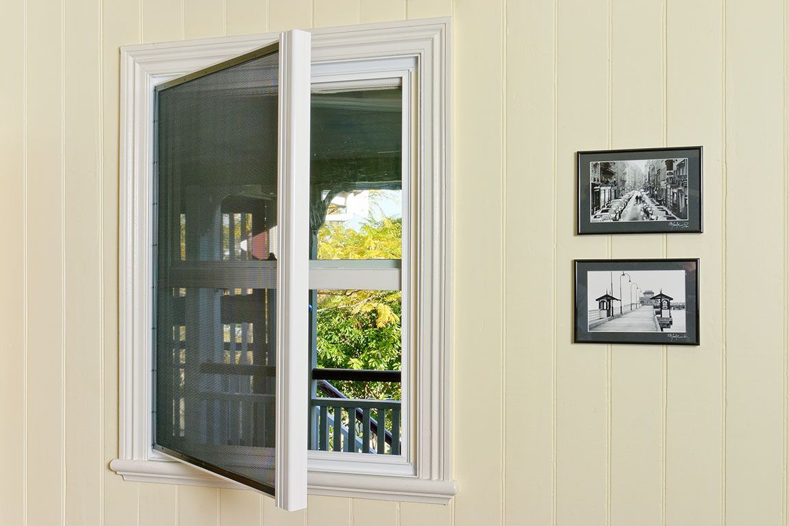 Open window with screen and white frame, showing a view of the outside and two framed photos on the wall.