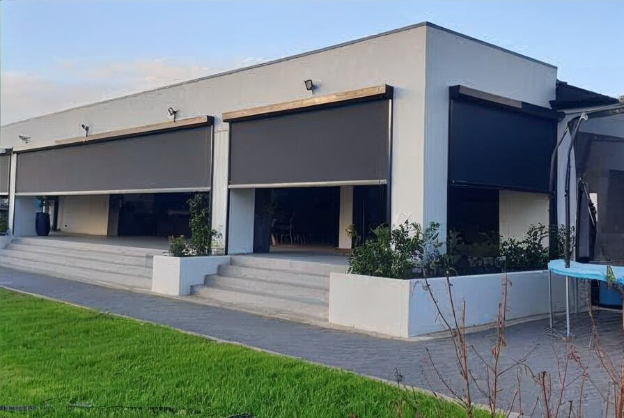 Family gathered on a patio for a barbecue. People are seated around a table and grilling.