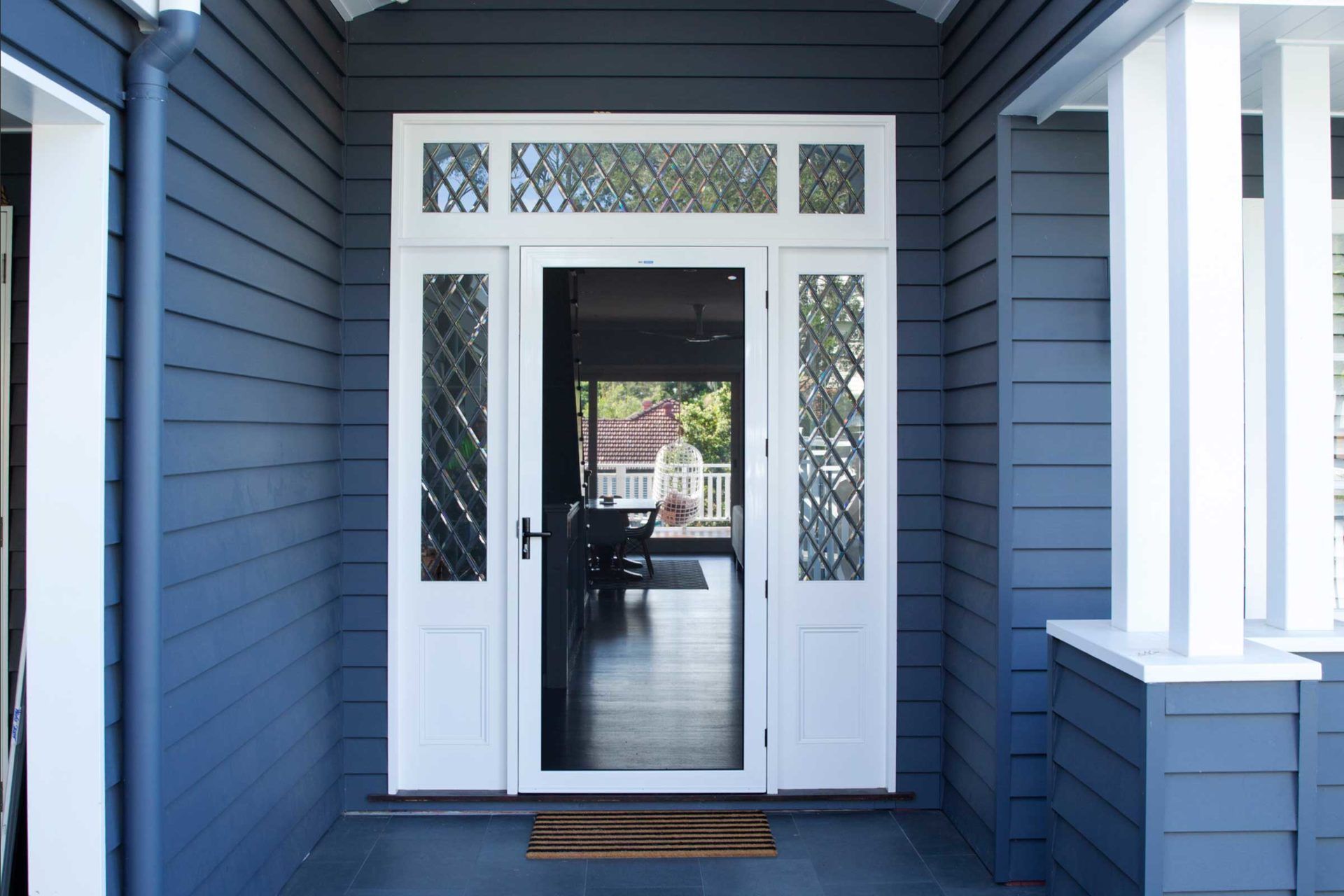 Blue exterior of a house, featuring white front door with sidelights and transom.