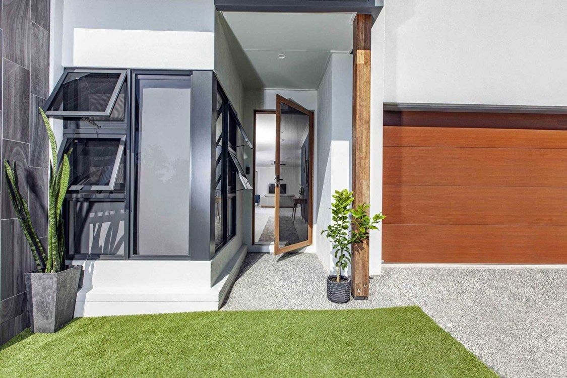 Exterior view of a modern home with windows, a garage door, and a small yard with artificial grass.