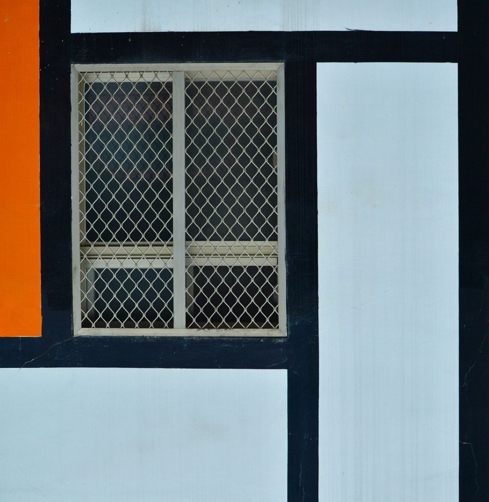 Window with a metal grid in a geometric design of black, orange, and white rectangles.