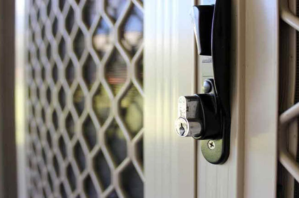 Close-up of a screen door with a black handle and a keyhole. The mesh screen is visible behind the lock.