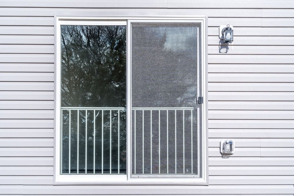 Sliding glass door with a metal railing, screen, and white siding. Two exterior lights and an outlet are mounted.