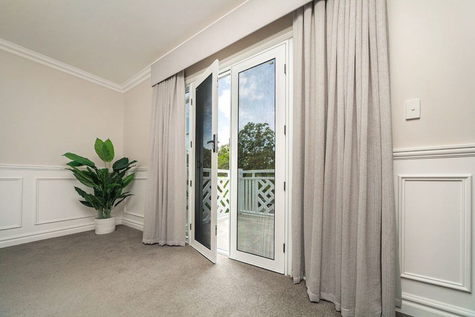 Room with French doors, light gray curtains, green plant, white trim, and a balcony view.