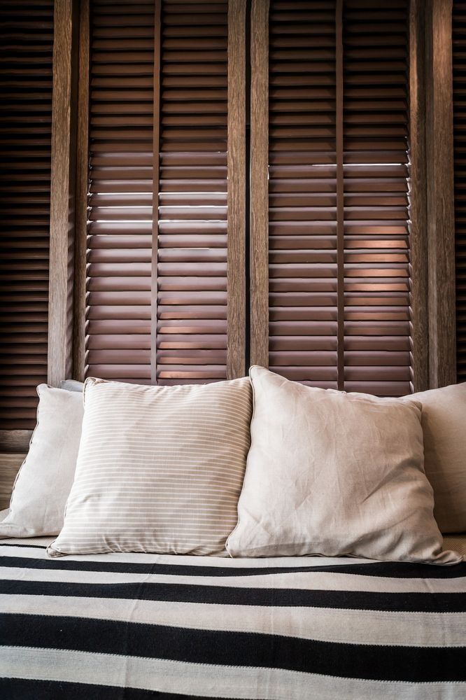 Cushions on a striped couch, against wooden shutters.