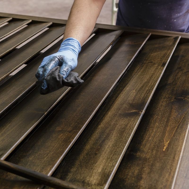 Woman on balcony, looking out, holding glass. White shirt, natural light. Small table, plants nearby.