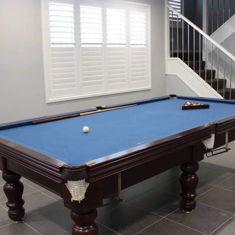 White and orange cat looking out a window with sunlight streaming through the blinds.