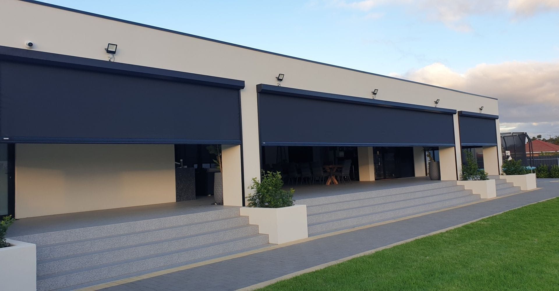 Modern building with blue awnings, steps, and green lawn. Cloudy sky in background.