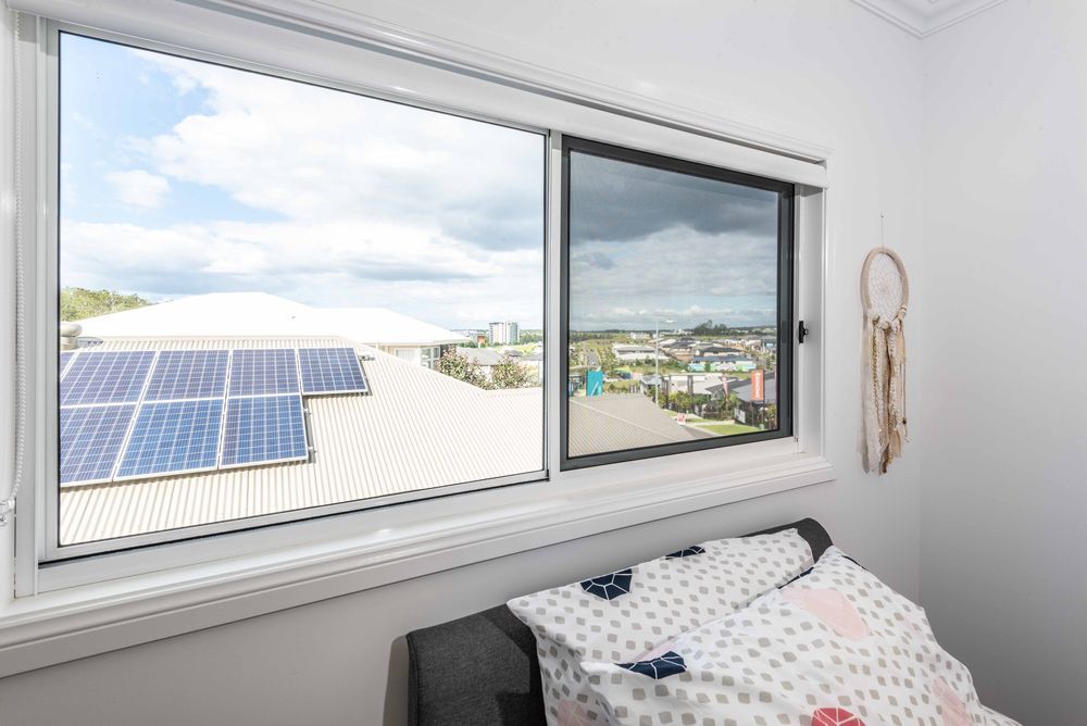 Window with solar panels on a rooftop and a dream catcher on the wall. Cloudy sky visible outside.