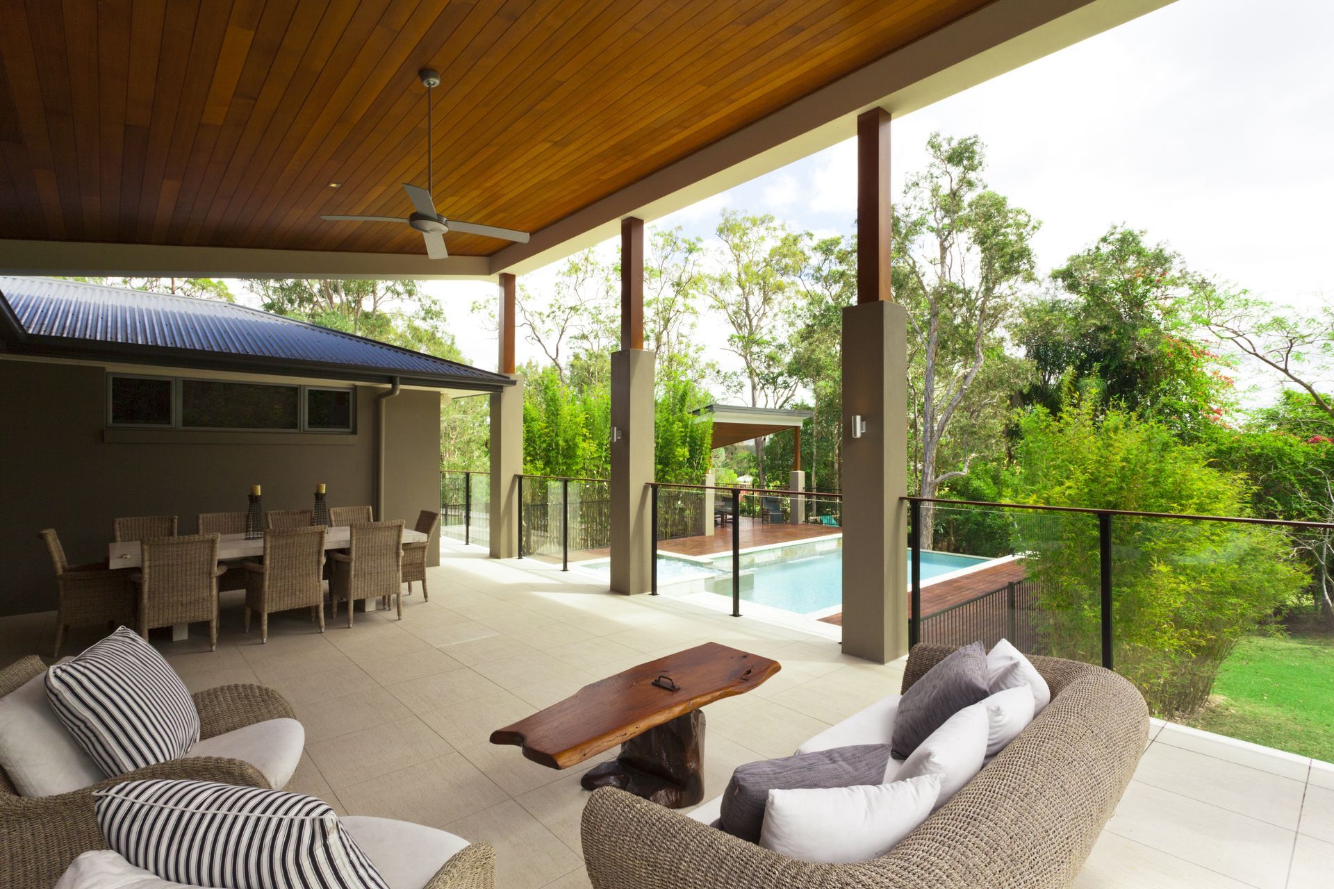 Covered patio with seating, dining area, and pool in a lush, green setting.