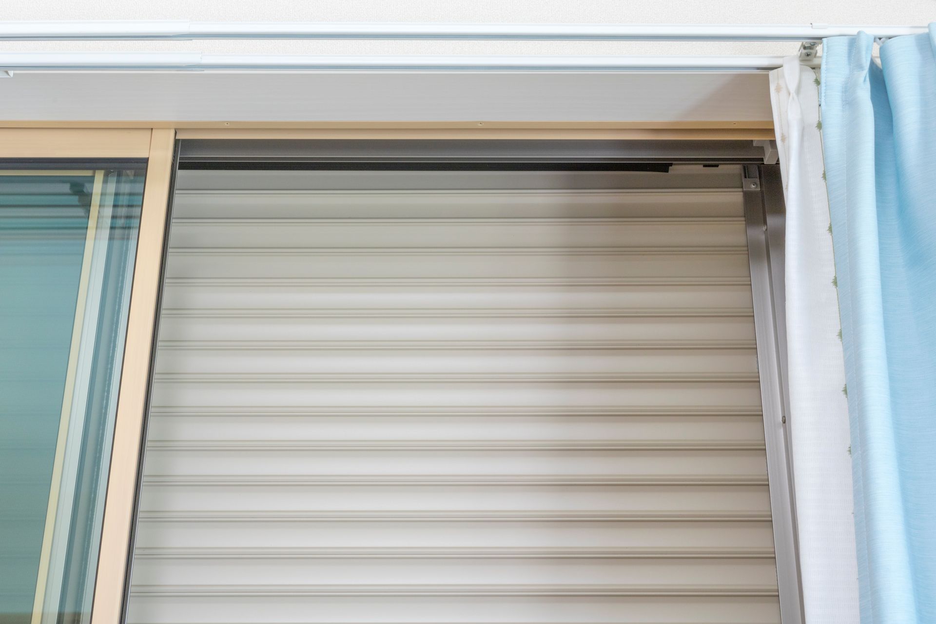 Window with closed horizontal blinds and a light blue curtain.