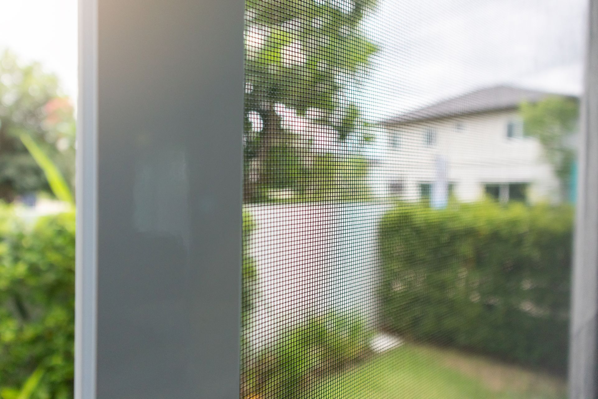 View of a house through a window screen. The screen is in focus, the house is blurred.
